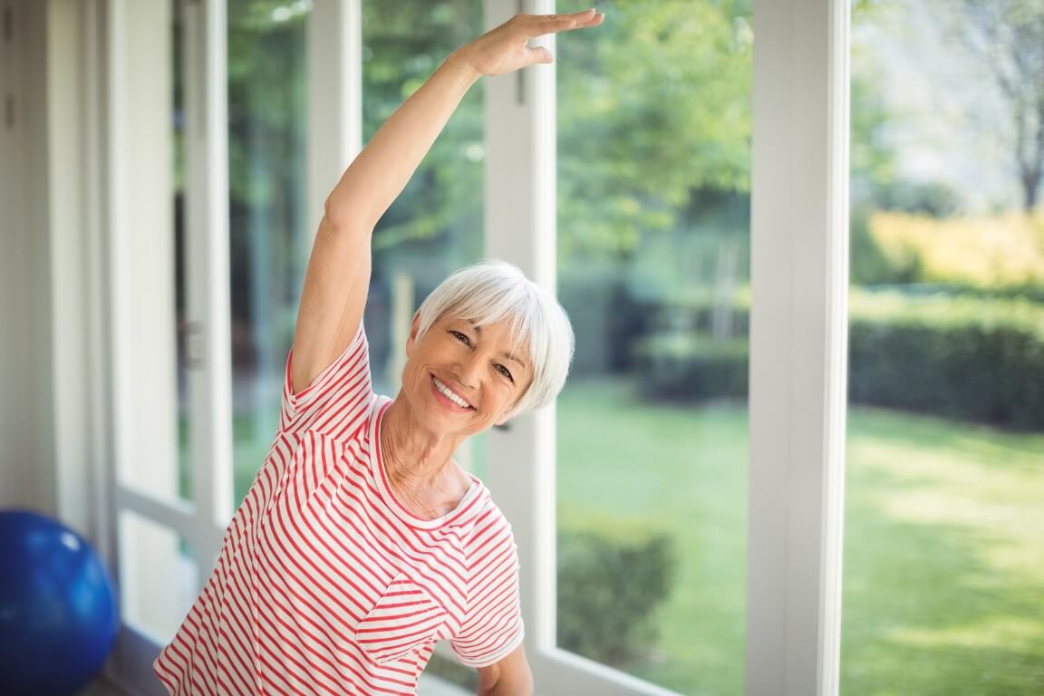 Portrait of happy senior woman performing stretching exercise